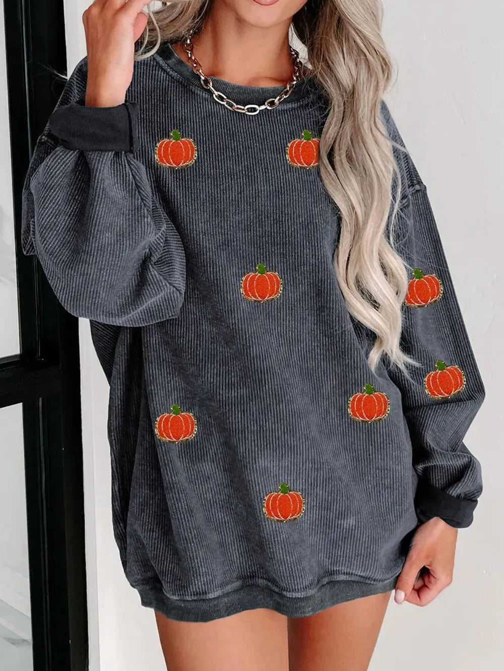 A woman wears a dark gray corduroy long-sleeve sweatshirt with pumpkin appliques.