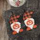 A pair of wooden dwarf pumpkin dangle earrings with orange and black plaid hats.