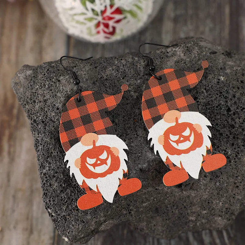 A pair of wooden dwarf pumpkin dangle earrings with orange and black plaid hats.