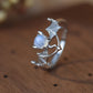 Sterling silver bat-wing ring with a central moonstone, resting on a wooden surface.