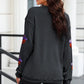 A woman from behind wears a black sequin pumpkin long sleeve sweatshirt and black shorts.
