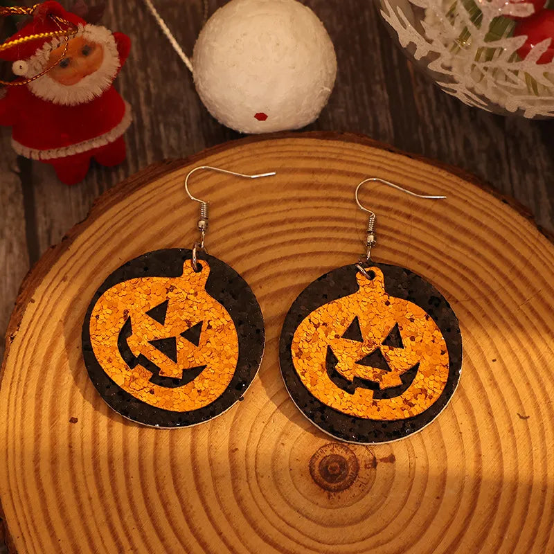 A pair of black and orange glitter pumpkin-shaped earrings on a wooden surface.