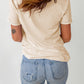 A woman from behind wears a beige short-sleeved t-shirt and light blue ripped jeans.