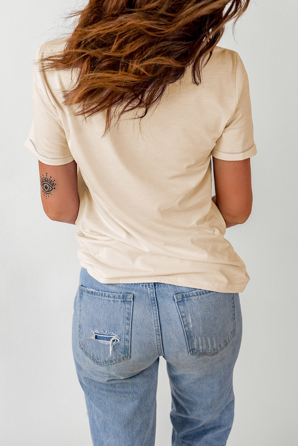 A woman from behind wears a beige short-sleeved t-shirt and light blue ripped jeans.