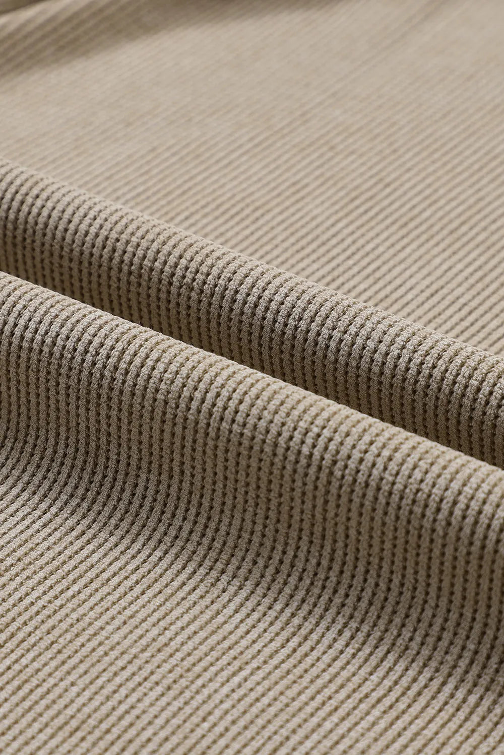 Close-up of beige corduroy fabric with visible ribs and folds.