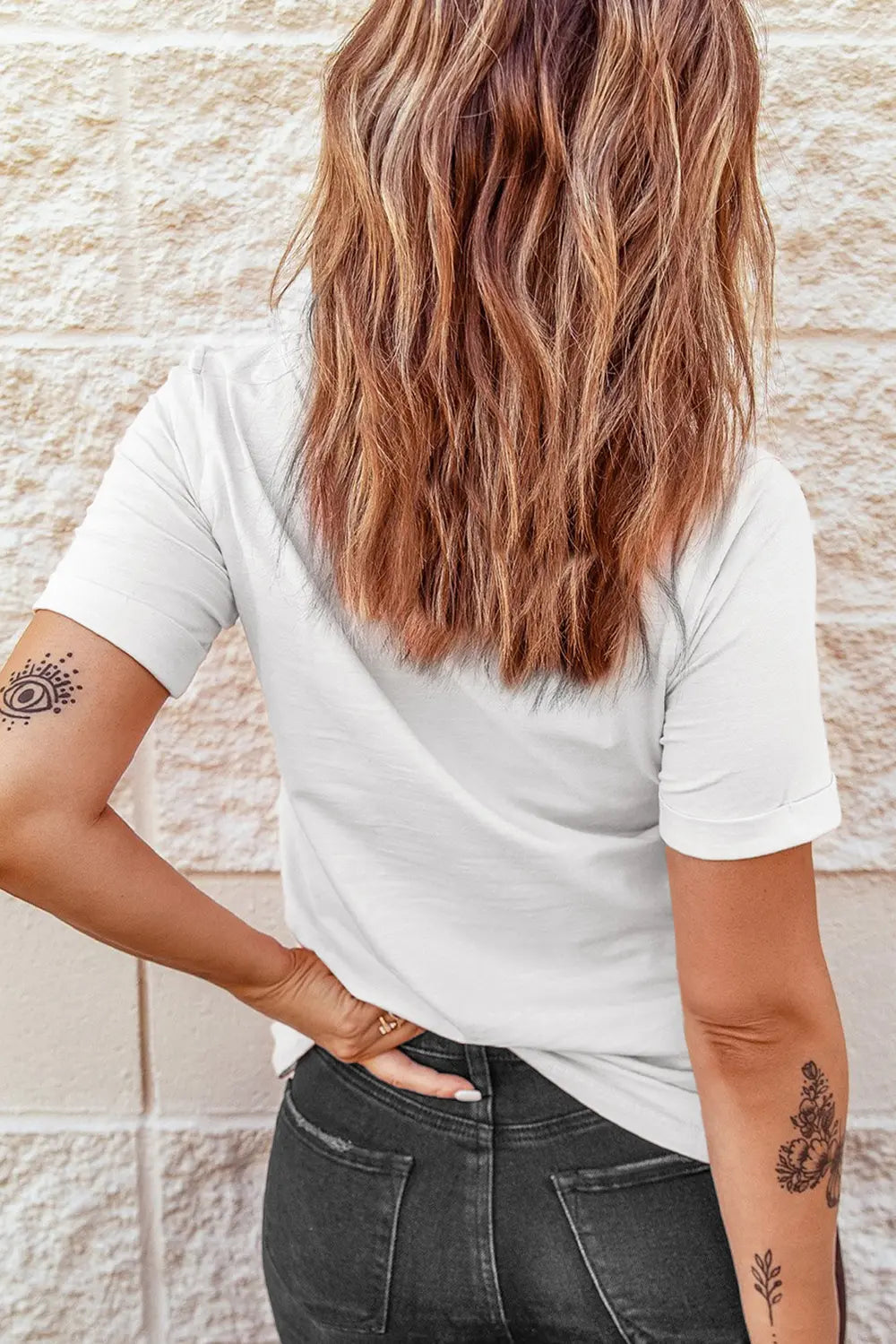 A woman from behind wears a white short sleeve t-shirt and dark jeans.
