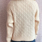 Cream cable-knit turtleneck sweater with long sleeves.