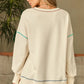 A woman models a cream long-sleeve sweatshirt with contrast stitching.