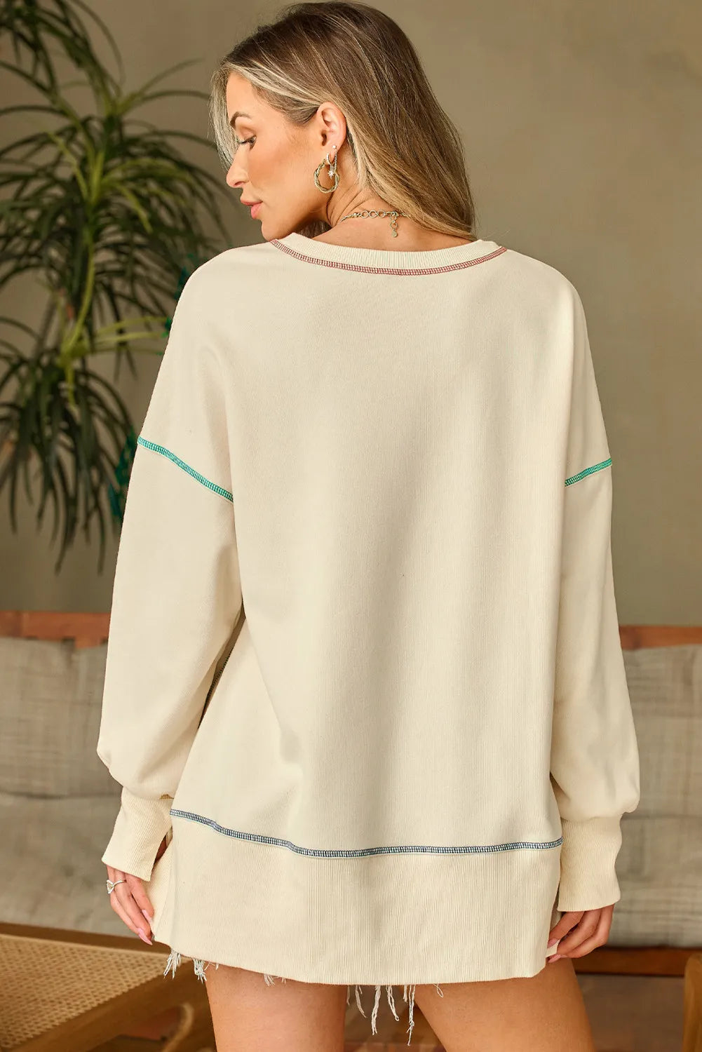 A woman models a cream long-sleeve sweatshirt with contrast stitching.