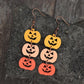 Wooden pumpkin earrings in yellow, light pink, and orange hang from copper hooks.