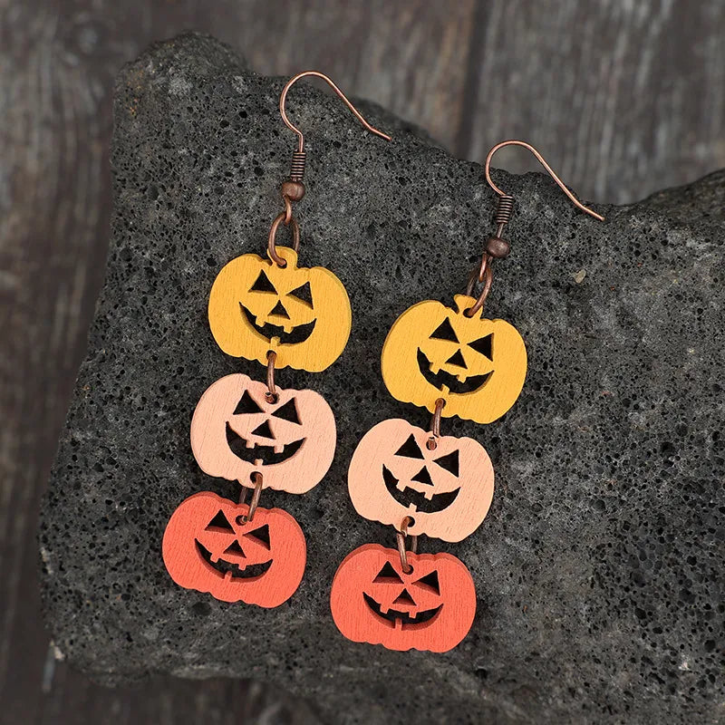 Wooden pumpkin earrings in yellow, light pink, and orange hang from copper hooks.