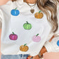 A woman wears a white long-sleeve sweatshirt with colorful sequin pumpkins.