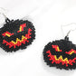 Two black, red, and yellow beaded Halloween pumpkin earrings are displayed on a white surface.
