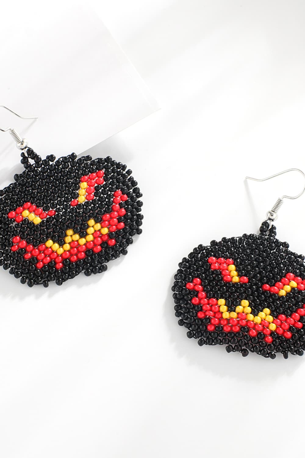 Two black, red, and yellow beaded Halloween pumpkin earrings are displayed on a white surface.