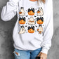 A woman wears a white long-sleeve sweatshirt with pumpkin and ghost graphics.