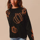 A woman models a black sweater with orange pumpkin outlines and a denim skirt.
