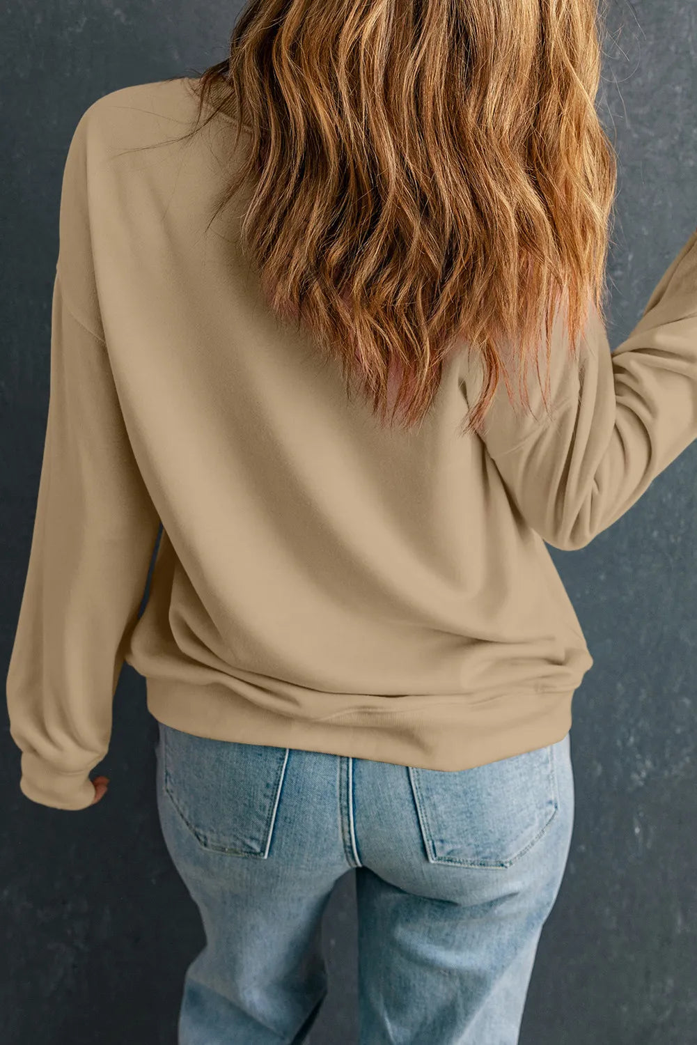 A woman from behind wears a long-sleeve pumpkin graphic sweatshirt and jeans.