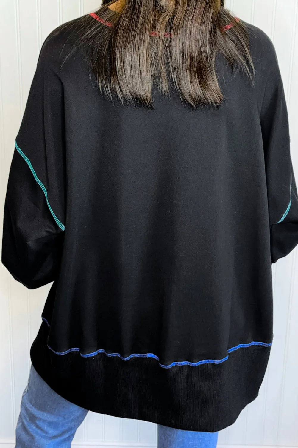 Black long sleeve sweatshirt with colorful stitching on the shoulders, sleeves, and hem.