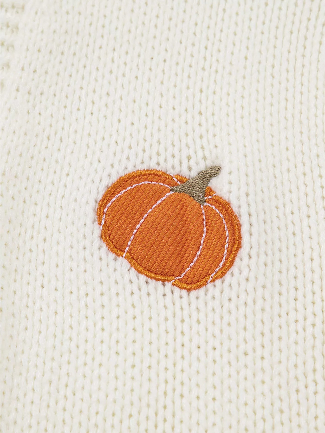 A close-up of a white knit cardigan with an embroidered orange pumpkin.
