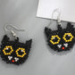 Two black beaded cat-shaped earrings with yellow eyes, white pupils, and a red nose.