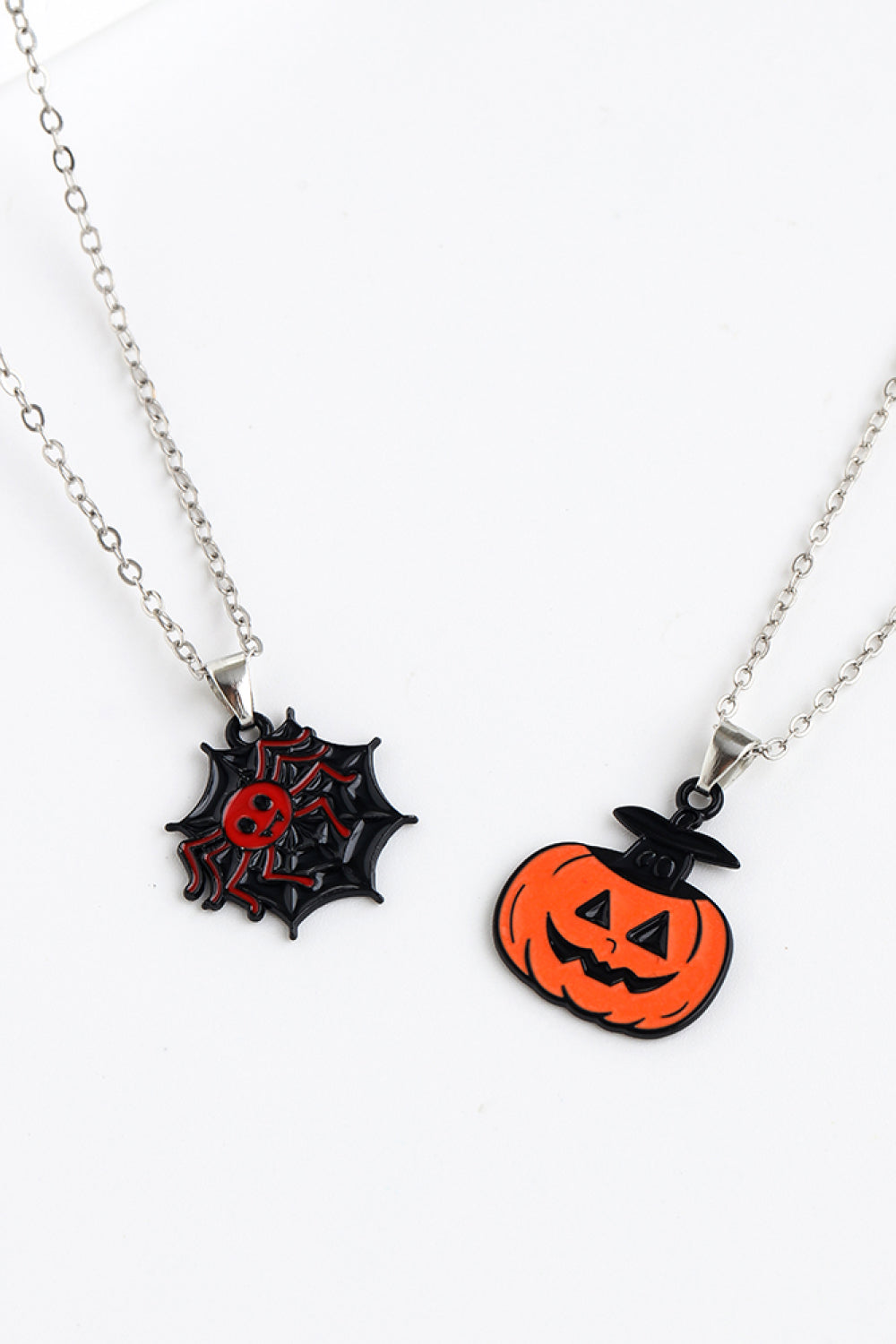 Two Halloween-themed necklaces, one with a spiderweb and spider, the other a jack-o'-lantern.