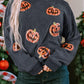 A woman wears a dark gray sequin patch pumpkin round neck sweatshirt and dark jeans.