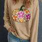 A woman wears a beige sweatshirt with a floral pumpkin graphic and blue jeans.