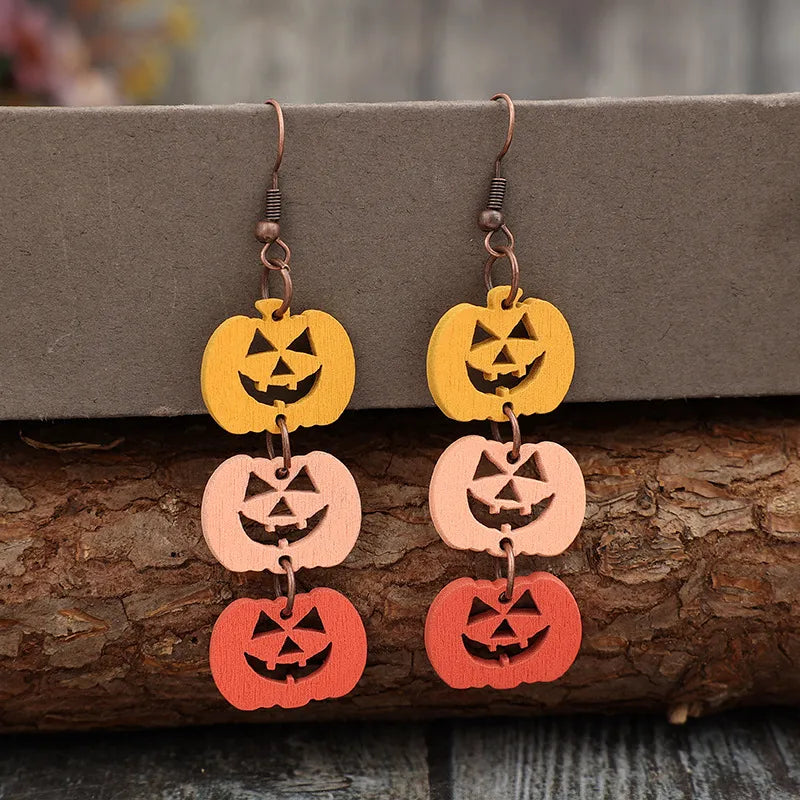 Wooden dangle earrings feature three carved pumpkins in yellow, light pink, and orange.