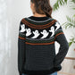 A woman from behind wears a black, orange, and green ghost-patterned sweater.