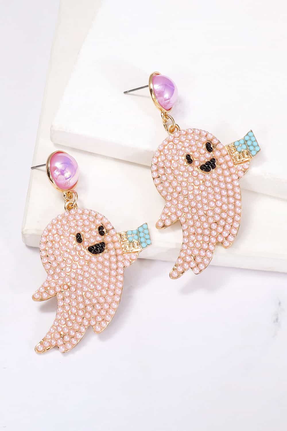Two pink pearl ghost dangle earrings with black faces and blue accents.