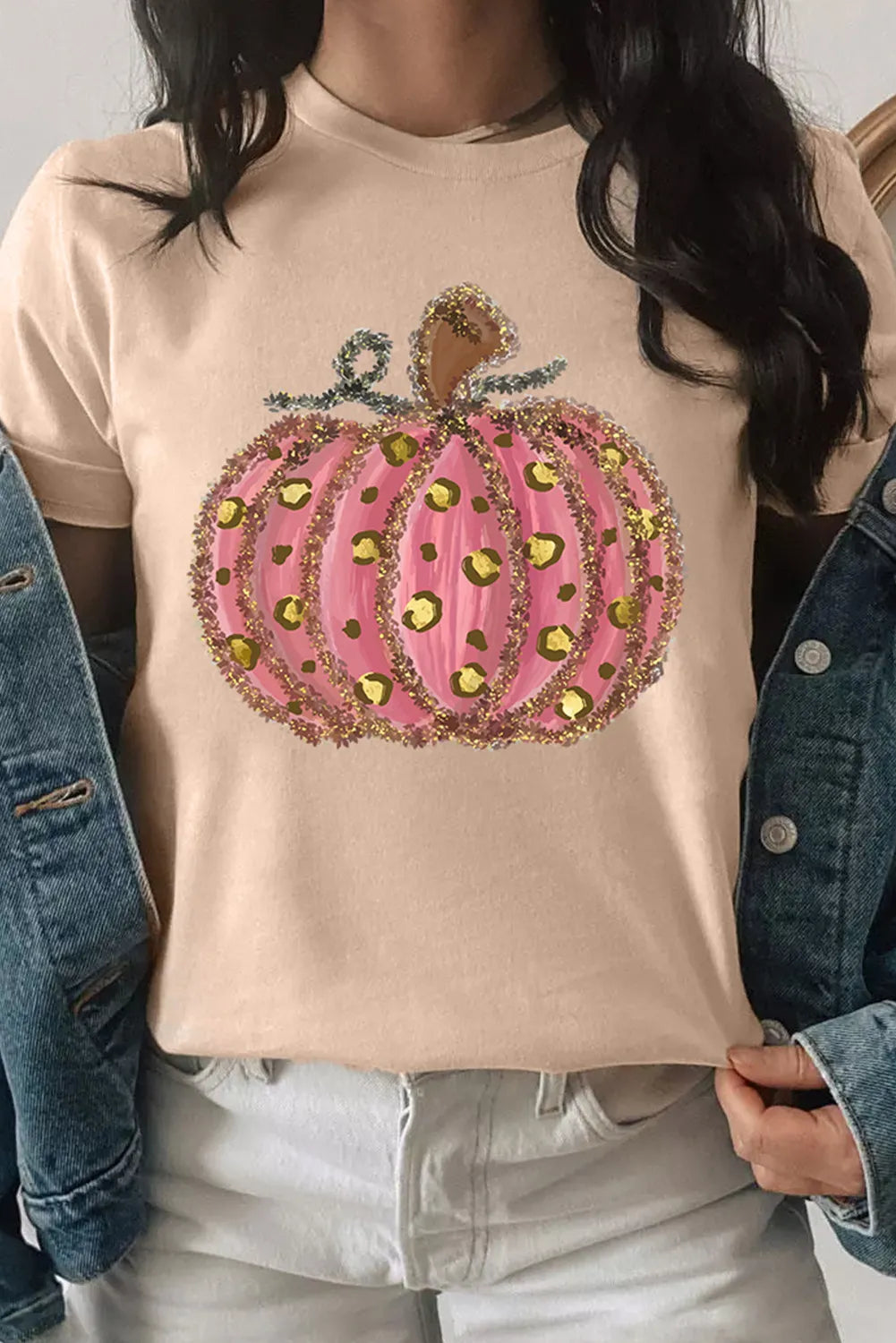 A woman wears a beige t-shirt with a pink, glittery, leopard-print pumpkin design.