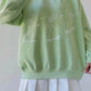 Oversized light green sweatshirt with white skeleton graphics and a white pleated skirt.