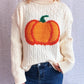 A woman wears a cream cable-knit turtleneck sweater with an orange pumpkin applique.