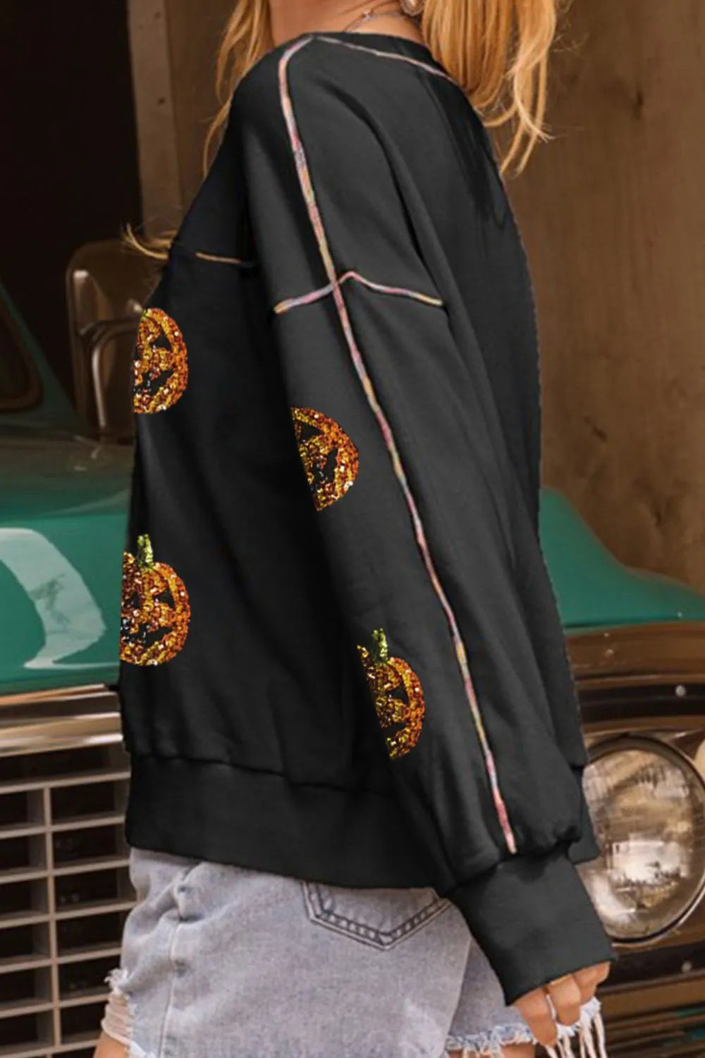 Black long-sleeve sweatshirt with sequin pumpkin designs and colorful shoulder piping.