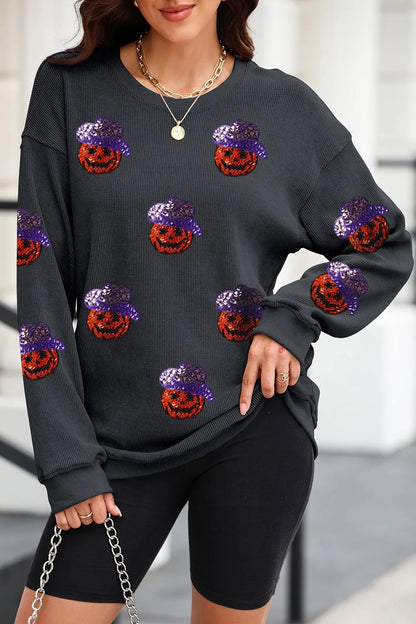 A woman wears a black long-sleeve sweatshirt with sequin pumpkin designs.