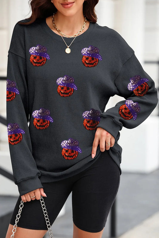 A woman wears a black long-sleeve sweatshirt with sequin pumpkin designs.