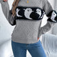 A woman wears a gray cable knit sweater with a black and white ghost pattern.