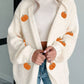 A woman wears an off-white knit cardigan with embroidered pumpkins.