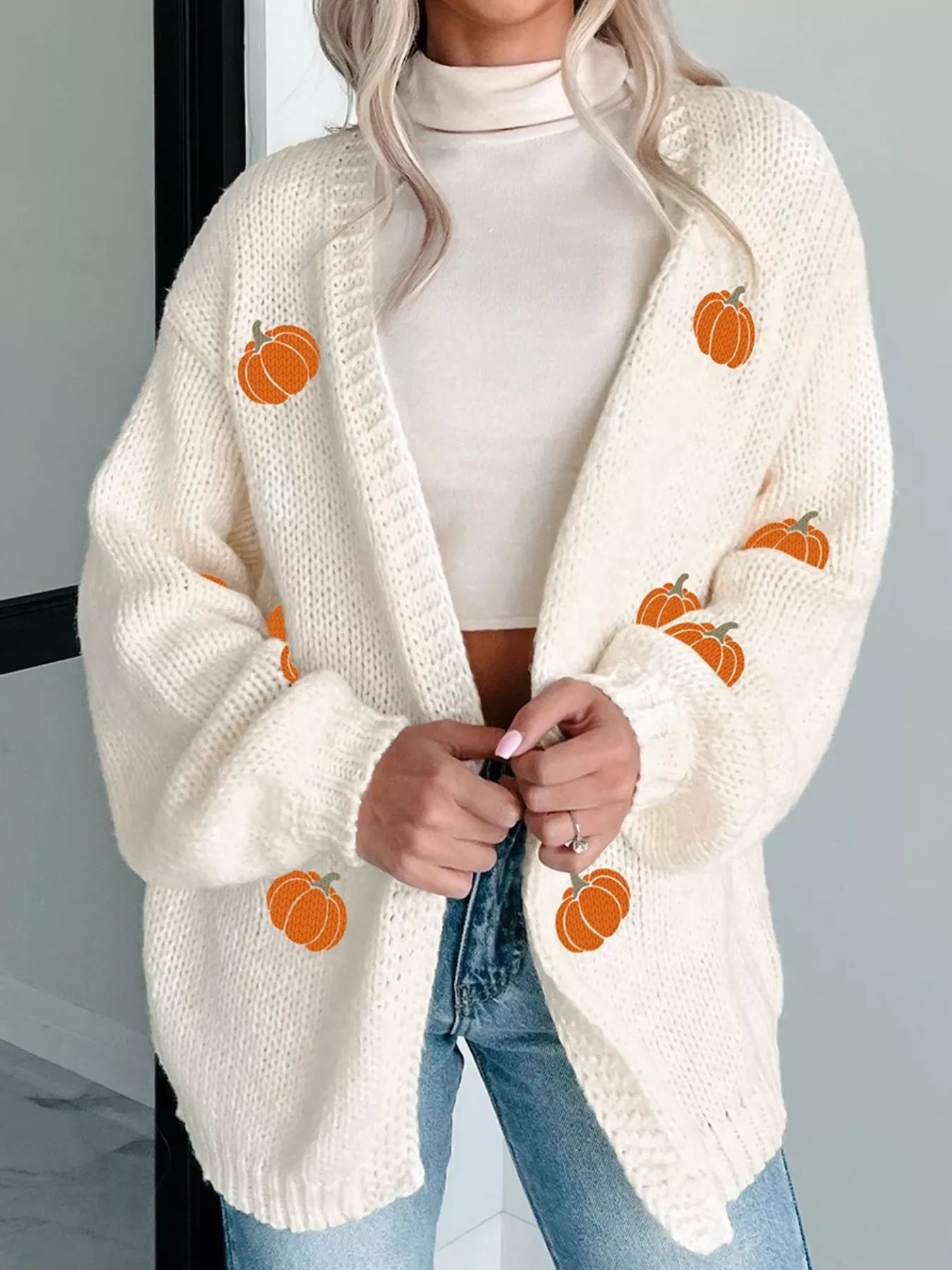 A woman wears an off-white knit cardigan with embroidered pumpkins.