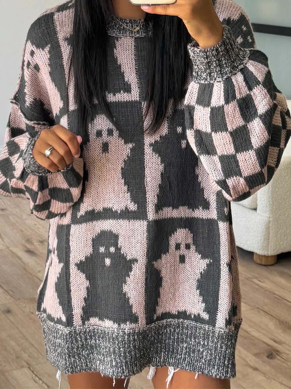 A person wears a pink and gray ghost-patterned dropped shoulder long sleeve sweater.