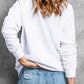 A woman from behind wears a white long-sleeve sweatshirt and distressed blue jeans.