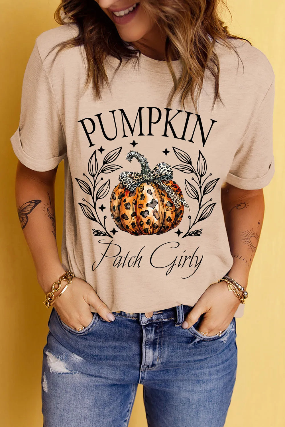 A woman wears a beige t-shirt with a "Pumpkin Patch Girly" graphic.
