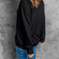 A woman from the back wearing a black long-sleeve sweatshirt and blue jeans.
