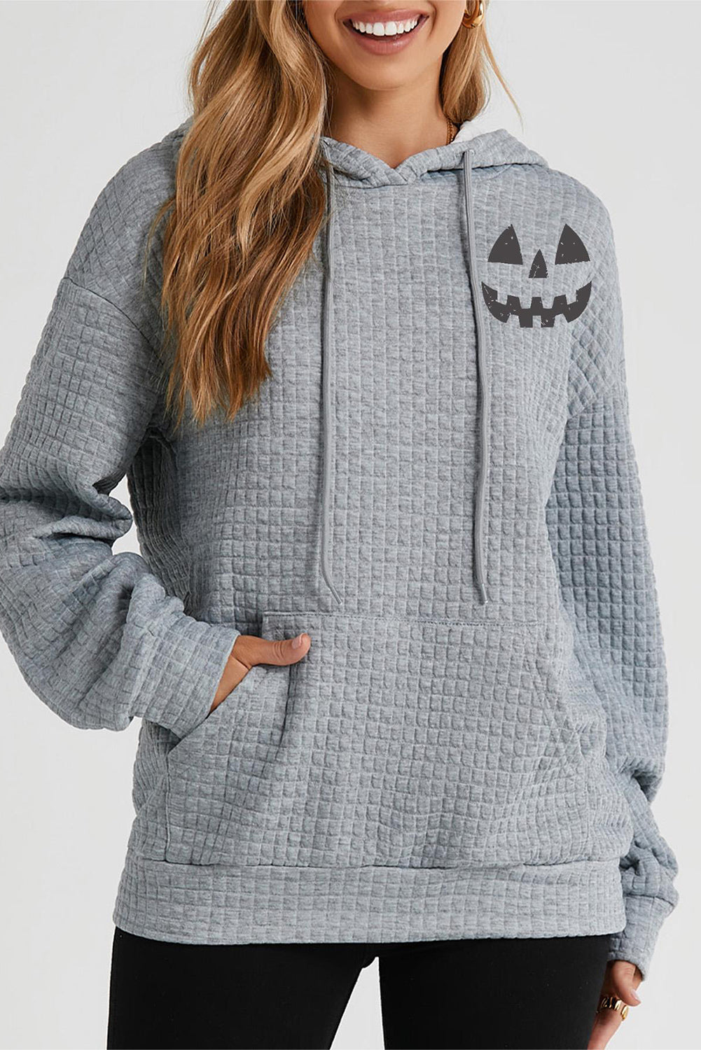 A woman wears a gray drawstring hoodie with a pumpkin face graphic and a front pocket.