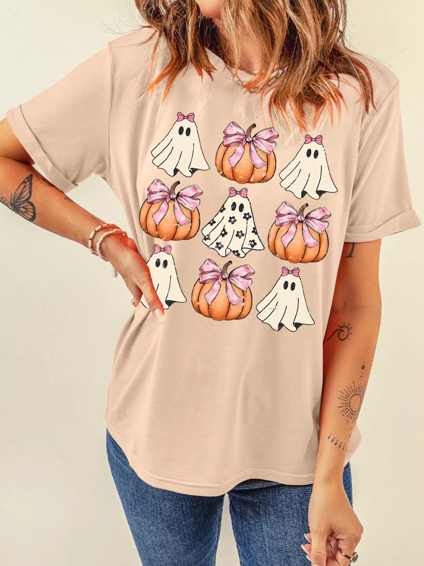 A woman wears a light pink t-shirt with a Halloween ghost and pumpkin graphic.
