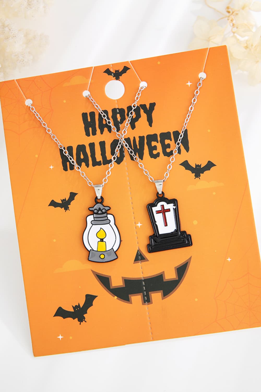 Two Halloween-themed necklaces, one with a lantern and one with a tombstone, on an orange card.