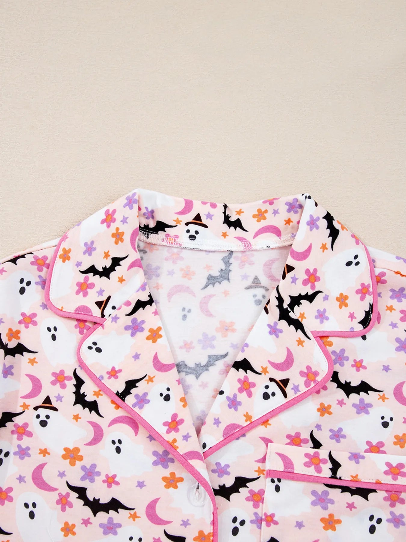 A pink Halloween ghost print button-up top with a collar and pink piping.