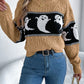 A woman wears a tan cable knit sweater with a black and white ghost pattern.