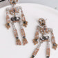 Skeleton-shaped dangle earrings adorned with clear, brown, and black glass stones.