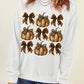 A woman wears a white long-sleeve sweatshirt with a pumpkin and bow graphic.